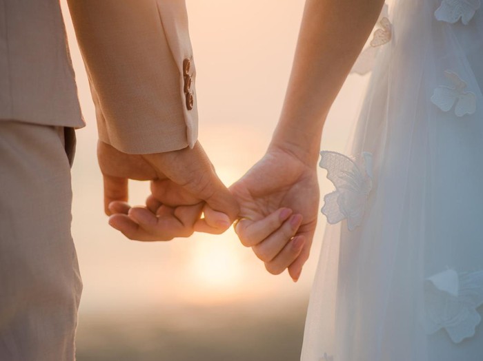 The bride and groom use the little finger together. lovely couple hold hand with sunset background