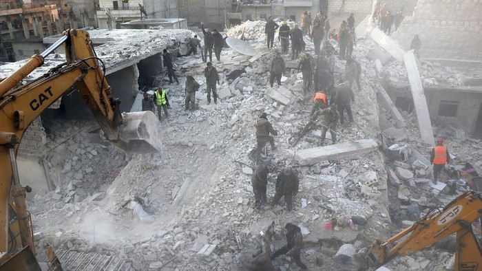 Penampakan Bangunan Runtuh yang Tewaskan Belasan Orang di Suriah In this photo provided by Kurdish-run Hawar News Agency, civil defense workers and civilians work on the rubble of a destroyed building in the Sheikh Maksoud neighborhood in Aleppo, Syria, Sunday, Jan. 22, 2023. The building collapsed in Aleppo early Sunday, killing at least 10 people, Syrian state media reported. (Hawar News Agency via AP)