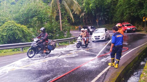 Petugas Damkartan Karangasem saat melakukan penyemprotan tumpahan oli di Jalan Raya Berina, Desa Tista, Selasa (24/1/2023).