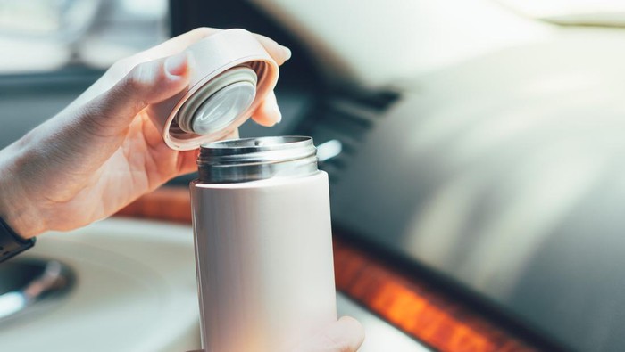 Close up of womans hands holding reusable insulated water bottle and opening the lid in car in bright sunlight