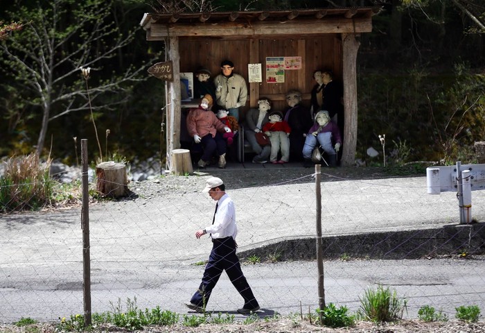 Seorang pria berjalan melewati shelter berisi boneka yang dibuat dengan tangan dan ditempatkan di sekitar desa oleh penduduk lokal Tsukimi Ayano untuk menggantikan populasi lokal yang semakin berkurang pada 22 April 2016 di desa Nagoro, di Miyoshi, Jepang.