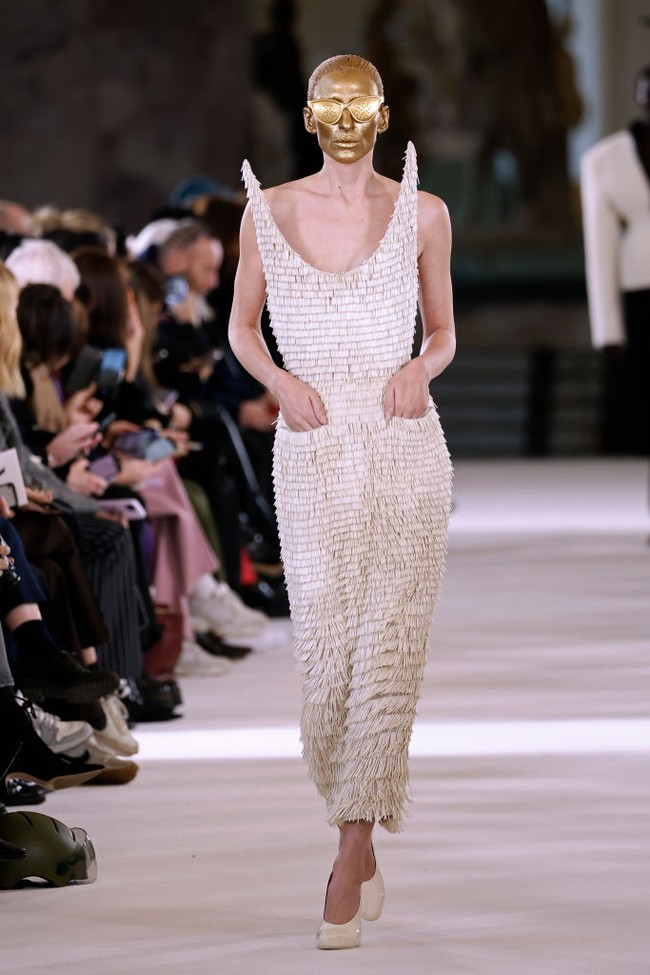 Membawakan gaun berdetail fringe, wanita 32 tahun ini tampil dengan wajah dipoles cat berwarna emas. Tampak kacamata melengkapi penampilannya. Foto: Getty Images/Estrop