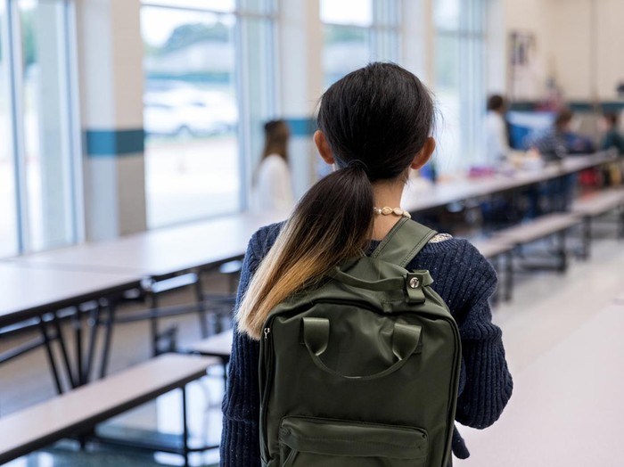 On the first day of school, the unrecognizable middle school girl carrying her backpack walks timidly into the cafeteria.