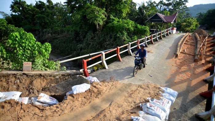 Jembatan di Padang Pariaman Rusak Diterjang Luapan Sungai Warga menggendong anaknya melintasi penyeberangan darurat di Nagari Sungai Buluh Timur, Kabupaten Padang Pariaman, Sumatera Barat Kamis (26/1/2023). Jembatan darurat yang dibangun masyarakat itu hancur akibat luapan Sungai Batang Anai dua hari lalu, sehingga warga kembali membuat penyeberangan darurat dari batang kelapa untuk akses antardesa. ANTARA FOTO/Iggoy el Fitra/rwa.