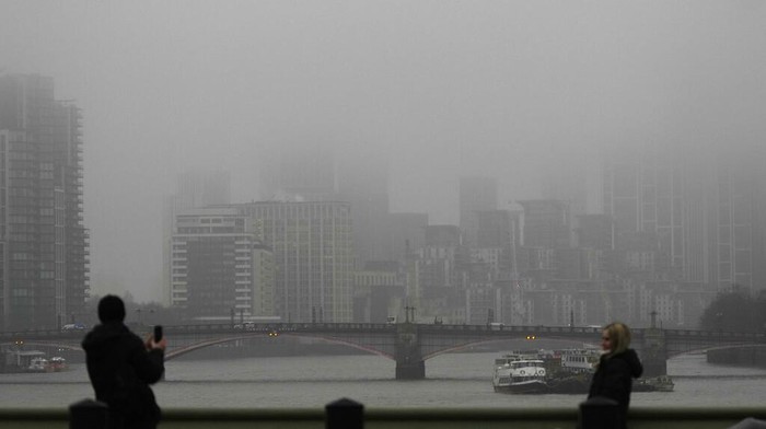 Tourist take pictures on their smart phones on Westminster Bridge looking west down the River Thames that is shouted in low cloud and mist in London, Wednesday, Jan. 25, 2023. (AP Photo/Alastair Grant)