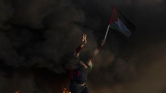 Asap Hitam Pejuang Palestina Lawan Pasukan Israel di Tepi Barat Palestinians burn tires and wave the national flag during a protest against Israeli military raid in the West Bank city of Jenin, along the border fence with Israel, in east of Gaza City, Thursday, Jan. 26, 2023. During the raid in the West Bank town of Jenin, Israeli forces killed at least nine Palestinians, including a 60-year-old woman, and wounded several others, Palestinian health officials said, in one of the deadliest days of fighting in years. The Israeli military said it was conducting an operation to arrest militants when a gun battle erupted. (AP Photo/Fatima Shbair)