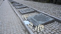 Lilin dan surat diletakkan di dekat batu peringatan di monumen Internasional untuk para korban. Ensiklopedia Holocaust/Holokaus mencatat lebih dari 1,1 juta orang tewas di Auschwitz. Para tahanan ditemukan mati dengan berbagai cara yang keji: dibunuh dengan gas beracun atau menjadi tahanan untuk kerja paksa. Getty Images/Omar Marques