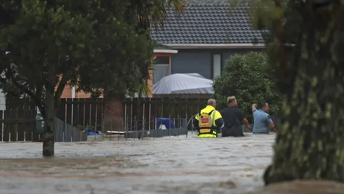 Emergency workers and a man wade through flood waters in Auckland, New Zealand, Friday, Jan. 27, 2023. Torrential rain and wild weather in Auckland causes disruptions throughout the city and an Elton John concert to be canceled just before it was due to start. (Hayden Woodward/New Zealand Herald via AP)