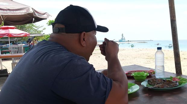 Salah seorang pengunjung, Made Simon dari Uluwatu tengah menyantap ikan bakar sambil menikmati keindahan pantai.