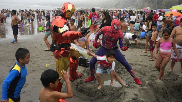Dua pria berkostum Spiderman dan Ironman bermain dan berswafoto bersama anak-anak yang ada di pantai.  
