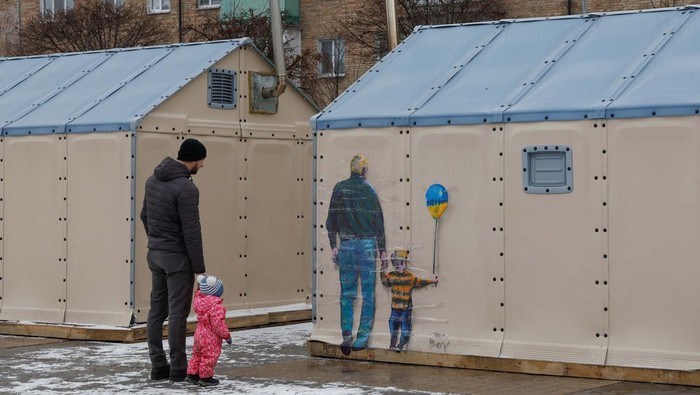 A man with a child looks an artwork of the famous street artist Tvboy, created on a wall of an 'invincibility centre', amid Russia's attack on Ukraine, in the town of Bucha, outside Kyiv, Ukraine January 29, 2023. REUTERS/Valentyn Ogirenko