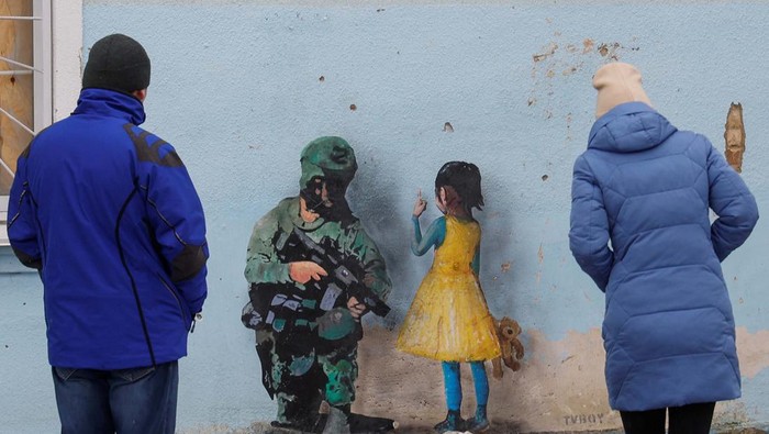 Seniman Jalanan Ini Bikin Karya Menarik di Tengah Perang Rusia-Ukraina A man with a child looks an artwork of the famous street artist Tvboy, created on a wall of an 'invincibility centre', amid Russia's attack on Ukraine, in the town of Bucha, outside Kyiv, Ukraine January 29, 2023. REUTERS/Valentyn Ogirenko