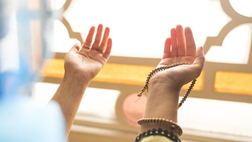 Muslim woman in headscarf and hijab prays with her hands up in air in mosque.Religion praying concept.