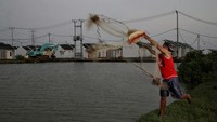 Seorang warga menjala ikan di danau yang tidak jauh dari sebuah kompleks perumahan.