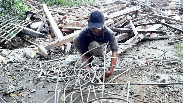 Adeng saat memungut besi reruntuhan rumahnya, imbas eksekusi lahan Tol Japek II Selatan
