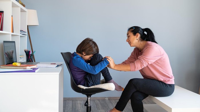 Photo of mother talking to her bored schoolboy son having online education during Coronavirus pandemic quarantine. Mother has black hair and is asian. Shot indoor with a full frame mirrorless camera.