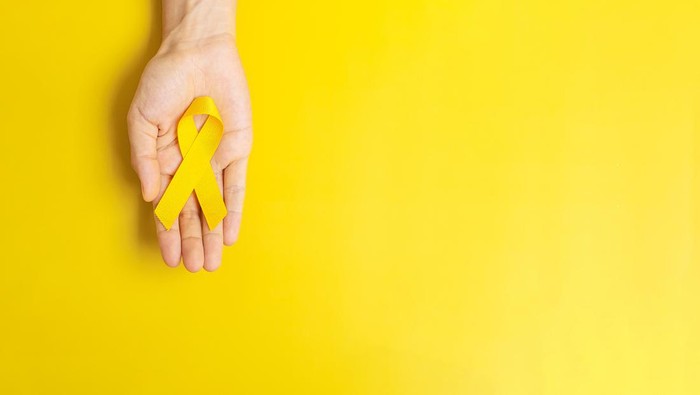 hand holding Yellow Ribbon on yellow background for supporting people living and illness. Suicide prevention day, Sarcoma cancer and Childhood Cancer Awareness month concept
