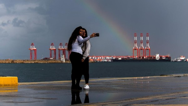 Dari Israel, dua orang wanita terlihat asyik swafoto dengan latar belakang penampakan pelangi di kawasan Mediterania, tepatnya di Pelabuhan Adani, Haifa, pada 31 Januari 2023 lalu. REUTERS/Amir Cohen