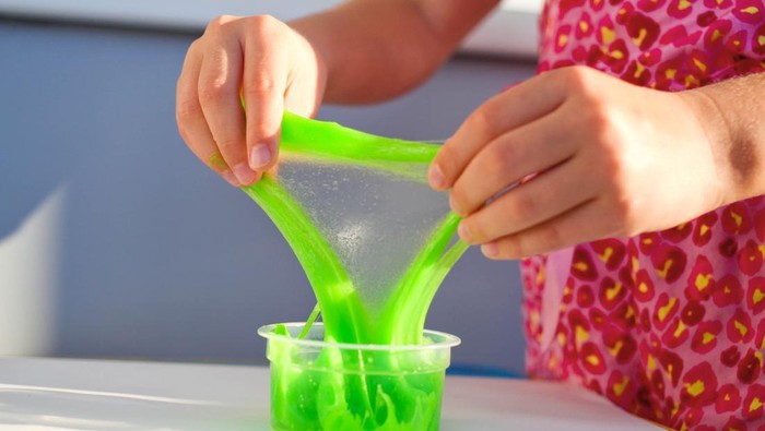 Hand holding homemade toy called Slime, kids having fun and being creative by science experiment. Close up of a little girl is hand playing a green slime