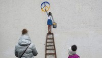 Sebuah mural menggambarkan seorang anak tengah melukis simbol perdamaian.  
