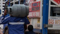 Seorang pria membawa tabung gas kosong melewati truk yang penuh dengan tabung gas yang kosong pula.  