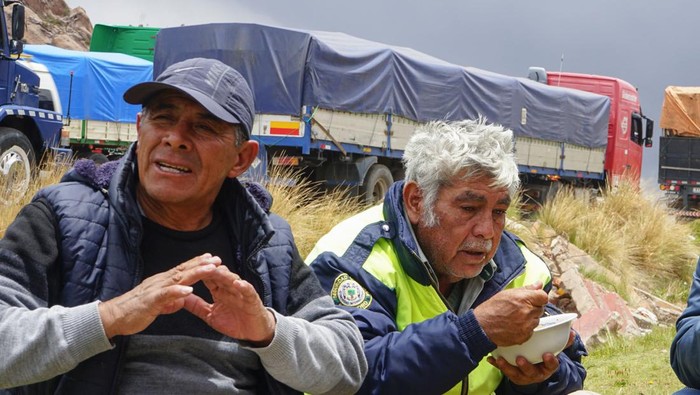 Ratusan Truk Terlantar Berhari-hari di Perbatasan Peru-Bolivia Truck drivers eat by their vehicles which remain lined up for days waiting for the road to Bolivia to open at the Desaguadero border pass in Peru on February 2, 2023. - More than 300 lorries are parked in parallel lines waiting for the end of the strike called by opposers to Peruvian President Dina Boluarte. The strike, effective in several regions of Peru, has affected the distribution and caused shortages of fuel, gas, water and food in several cities in the southeast of the country. (Photo by Bernat BIDEGAIN / AFP) (Photo by BERNAT BIDEGAIN/AFP via Getty Images)