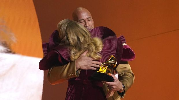 Dwayne Johnson, in the back, embraces Adele after presenting the award for best pop solo performance for 
