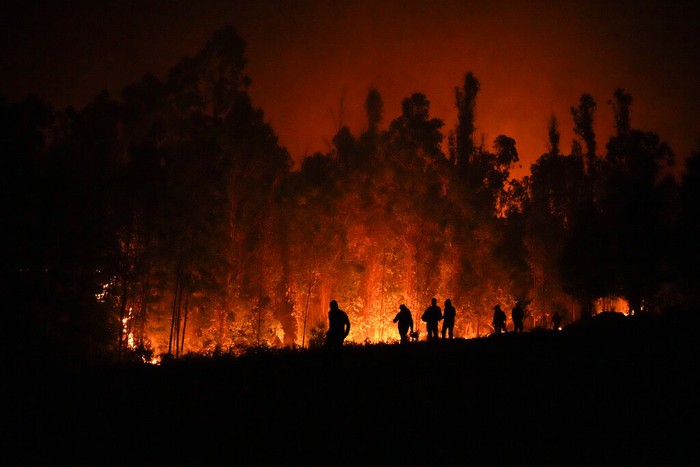 Volunteers carry supplies for firefighters near trees burning in Puren, Chile, late Saturday, Feb. 4, 2023. Forest fires are spreading in southern and central Chile, triggering evacuations and the declaration of a state of emergency in some regions. (AP Photo/Matias Delacroix)