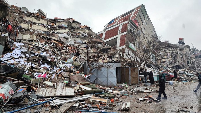 People stand in front of collapsed buildings following an earthquake in Kahramanmaras, Turkey February 6, 2023. Ihlas News Agency (IHA) via REUTERS ATTENTION EDITORS - THIS PICTURE WAS PROVIDED BY A THIRD PARTY. NO RESALES. NO ARCHIVES. TURKEY OUT. NO COMMERCIAL OR EDITORIAL SALES IN TURKEY.