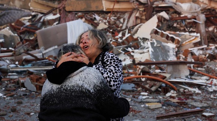 People sit amid rubble following an earthquake in Hatay, Turkey, February 7, 2023. REUTERS/Umit Bektas