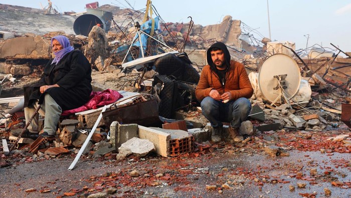 People sit amid rubble following an earthquake in Hatay, Turkey, February 7, 2023. REUTERS/Umit Bektas