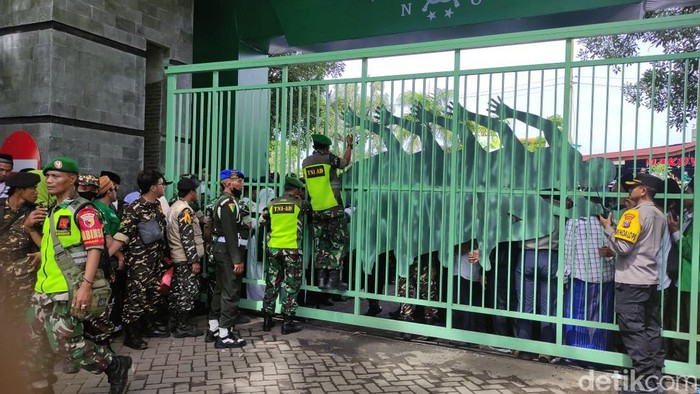 Seorang anggota Banser tampak memanjat pagar memperingatkan jemaah agar tidak berdesakan karena ada anak kecil