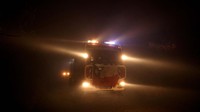 Mobil pemadam kebakaran menembus gelap hutan yang tertutup asap kebakaran.