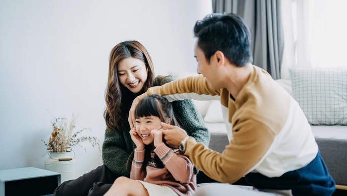 Young family having fun at home while father pinching daughters cheek and laughing joyfully