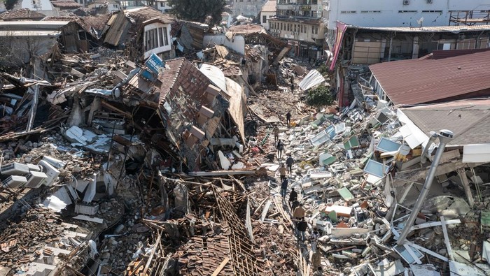 HATAY, TURKEY - FEBRUARY 08: People walk past collapsed buildings on February 08, 2023 in Hatay, Turkey. A 7.8-magnitude earthquake hit near Gaziantep, Turkey, in the early hours of Monday, followed by another 7.5-magnitude tremor just after midday. The quakes caused widespread destruction in southern Turkey and northern Syria and were felt in nearby countries. (Photo by Burak Kara/Getty Images)
