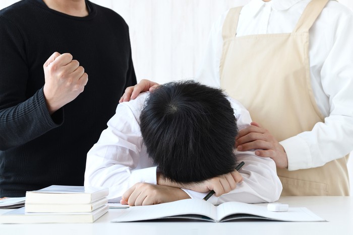 Boy lying face down on desk and encouraging parents