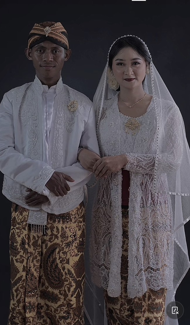 Kisah pengantin beda warna kulit ini viral usai Arum Puspitasari sang pengantin wanita membagikan momen pernikahannya lewat akun TikTok @arumpps. Dalam video terlihat Arum dan suaminya sedang berada di pelaminan. Arum juga memperlihatkan foto saat memakai kebaya putih adat Jawa. Sedangkan suaminya yang asal Jawa dengan akun @jitengwongjowo, mengenakan blankon dan beskap putih. Foto: Dok. TikTok @arumpps.