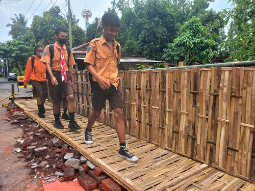 Sejumlah pelajar terlihat melintasi jembatan darurat yang dibuat swadaya oleh masyarakat menggunakan bambu, Jumat (10/2/2023). (Made Wijaya Kusuma)