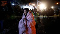Seorang wanita menutupi dengan selimut saat anggota tim penyelamat mencari korban yang selamat setelah gempa mematikan di Kirikhan, Turki. Korban gempa juga kini dihadapkan dengan cuaca dingan. REUTERS/Guglielmo Mangiapane.