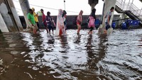 Sejumlah warga melintasi jalanan yang tergenang banjir.