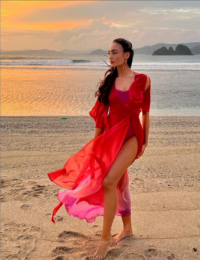 Dalam kesempatan lain, R’Bonney Gabriel juga berfoto dengan latar belakang pantai Lombok yang indah. Wanita yang berprofesi sebagai desainer ini tampak menhenakan swimsuit pink yang dipadu gaun transparan merah. Foto: Instagram/@rbonneynola