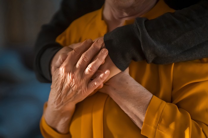 A young man, a volunteer, a son carefully hugs his beloved grandmother, supports and helps an elderly woman in retirement, his grandparent. Young male and female elderly hands with wrinkles closeup.