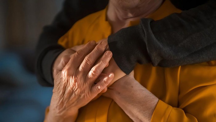 A young man, a volunteer, a son carefully hugs his beloved grandmother, supports and helps an elderly woman in retirement, his grandparent. Young male and female elderly hands with wrinkles closeup.