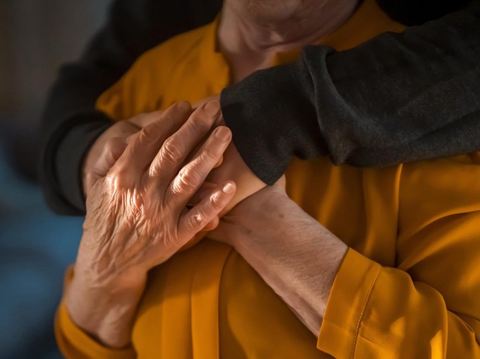 A young man, a volunteer, a son carefully hugs his beloved grandmother, supports and helps an elderly woman in retirement, his grandparent. Young male and female elderly hands with wrinkles closeup.