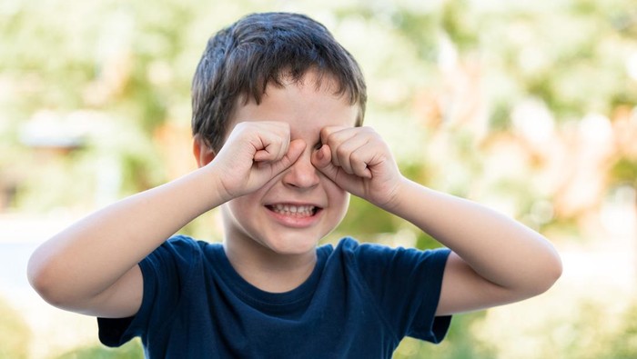 Child suffering itching scratching eyes outdoors in a park