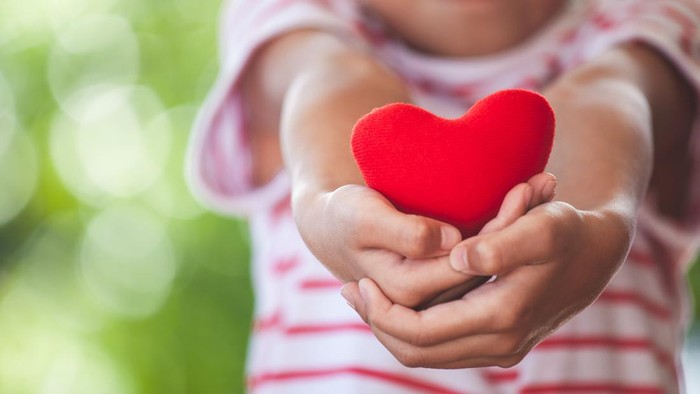 Cute asian little child girl showing and holding red heart in hand with care and love
