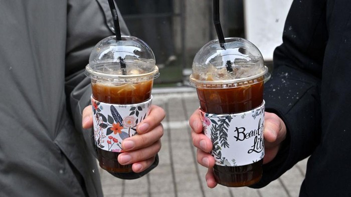 Kopi Americano yang Begitu Digemari Warga Korea Selatan This picture taken on January 26, 2023 shows people holding iced Americanos during an interview with AFP on a street in Seoul. - K-pop stars BTS drink it. It appears in K-dramas. Fans are so dedicated to consuming it year-round they've coined a new South Korean proverb: