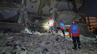 Berbekal lampu senter, tim SAR menyusuri reruntuhan bangunan untuk mencari korban gempa. Shenzhen Rescue Volunteers /Handout/Anadolu Agency/Getty Images.
