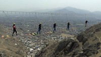 Orang-orang melintasi jembatan gantung di atas distrik San Juan de Lurigancho di Lima, Peru, Minggu (12/2/2023).