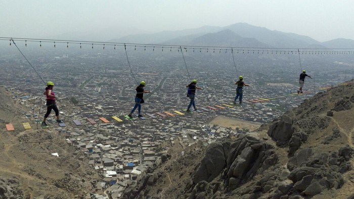 People cross a suspension bridge over the San Juan de Lurigancho district in Lima, Peru, Sunday, Feb. 12, 2023. Peruvians have found ways to manage their daily lives even as police and protesters clash across the country amid political turmoil over the removal of former President Pedro Castillo, who was later arrested for trying to dissolve Congress. (AP Photo/Guadalupe Pardo)